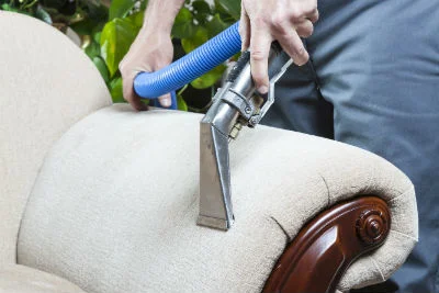 Technician using hot water extraction equipment to clean upholstered furniture with blue hose attachment