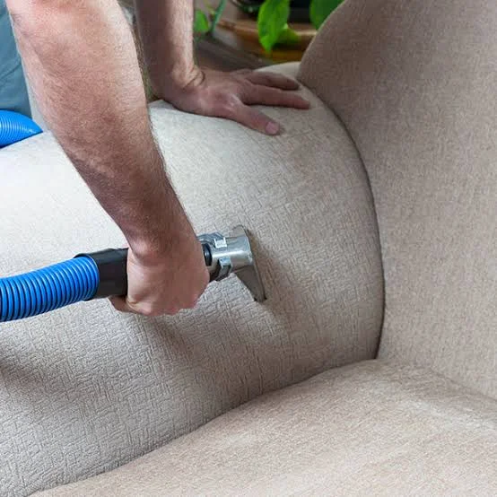 Technician cleaning beige upholstered chair with hot water extraction hose and attachment