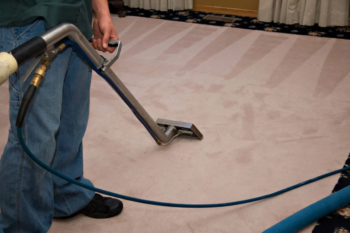 Technician using hot water extraction wand on light-colored residential carpet