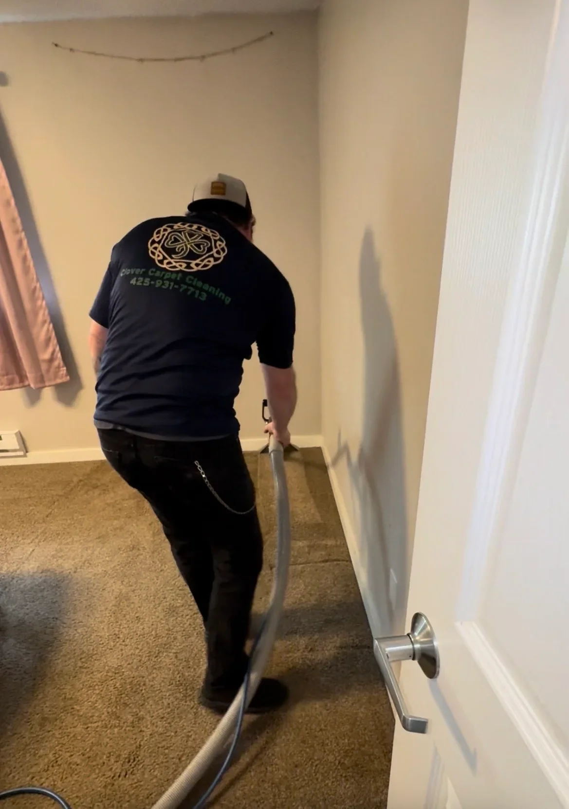Technician performing hot water extraction carpet cleaning with truck-mounted equipment and hose