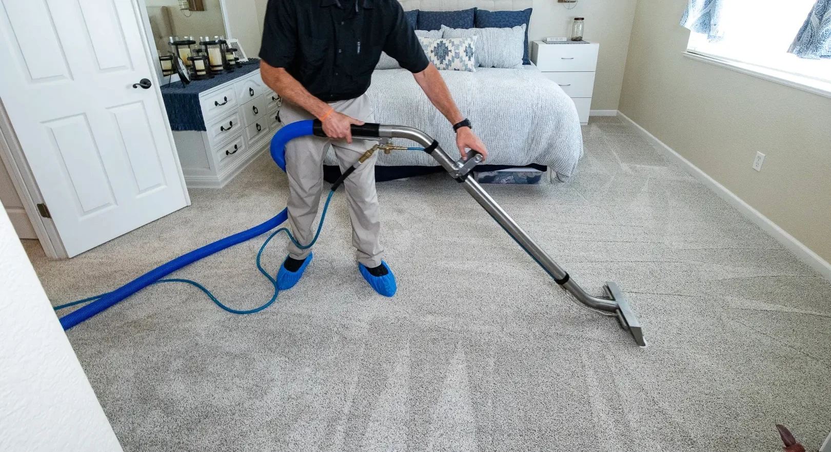 Technician performing hot water extraction carpet cleaning in bedroom with wand equipment