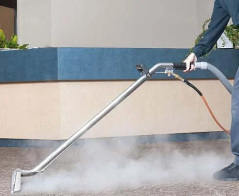 Technician using hot water extraction wand on carpet with steam visible